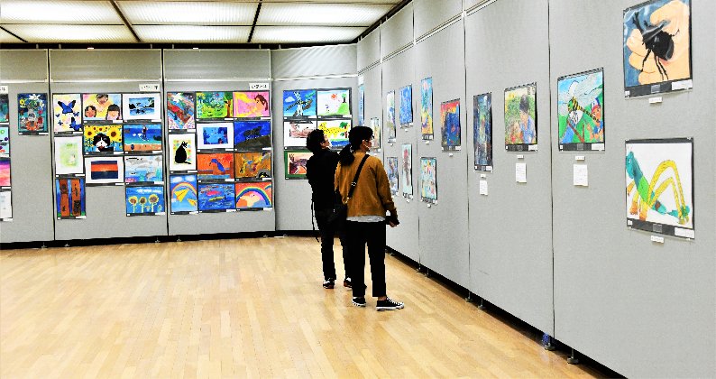 パネルに展示されている市展絵画の部(子ども)の絵を鑑賞している来場者の方の写真