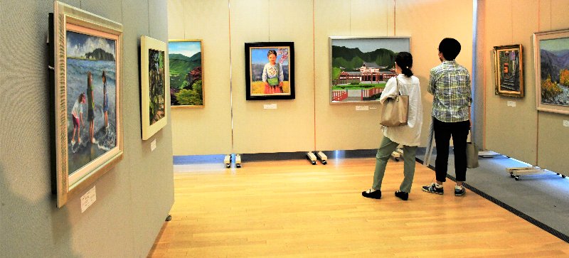 2名の来場者が、パネルに展示されている額縁に入った絵画を鑑賞している写真
