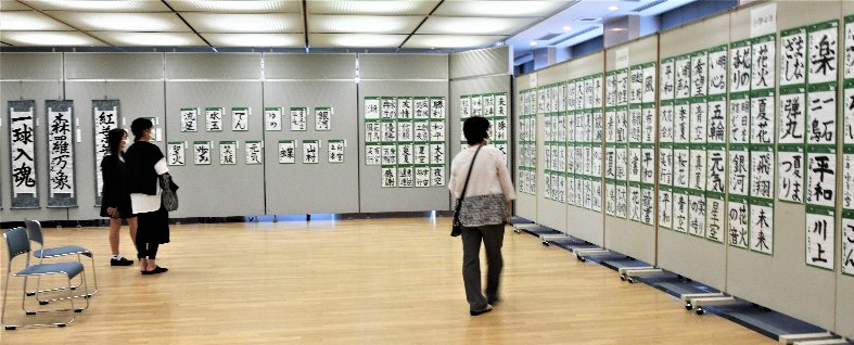 パネルに展示されている沢山の書を鑑賞している人たちの写真 拡大画像
