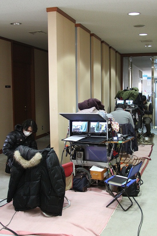 通路の左側の床の上に置かれた機材のなかで作業をしているスタッフの人達の写真
