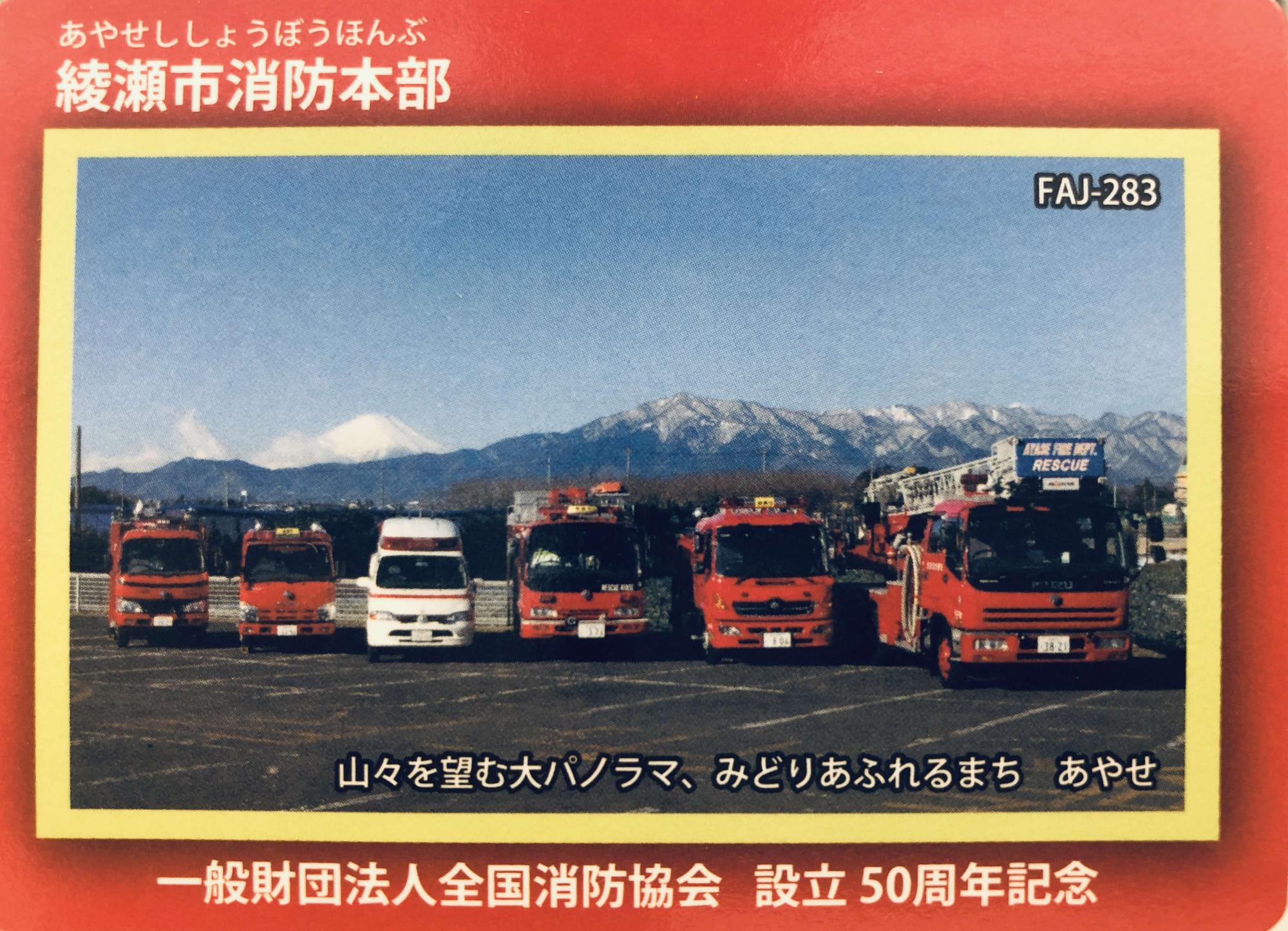 綾瀬市消防本部 山々を望む大パノラマ、みどりあふれるまち あやせ 一般財団法人全国消防協会 設立50周年記念 の文字と後方に山々がうつり、色々な種類の消防車や救急者が並んでいる綾瀬市消防本部カードの表面