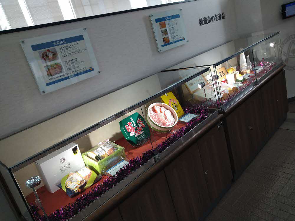 綾瀬市の名産品が展示されているショーケースと壁に掲示された商品の紹介パネルの写真