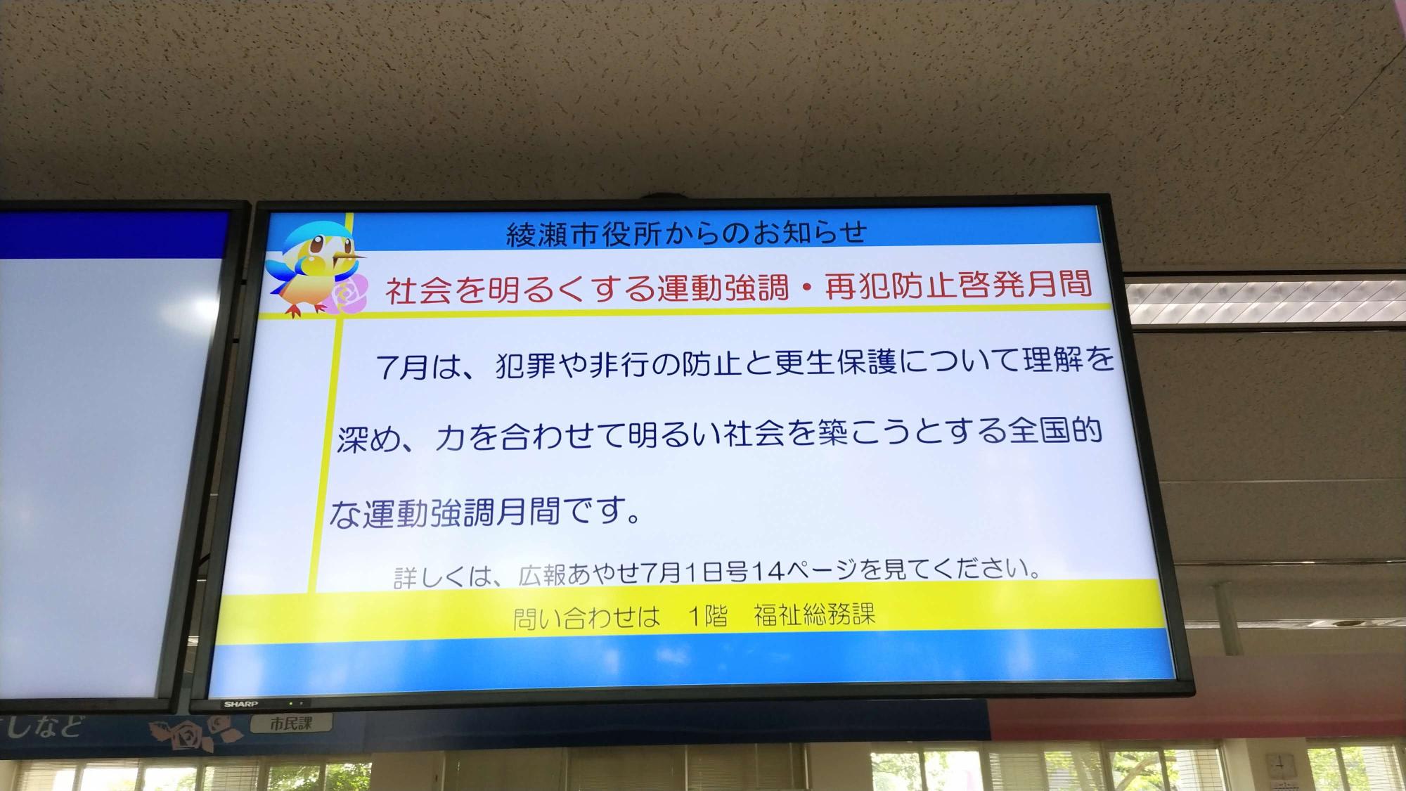 市民課窓口ナンバーモニターの横の画面に「社会を明るくする運動」の案内コマーシャルが流れている写真