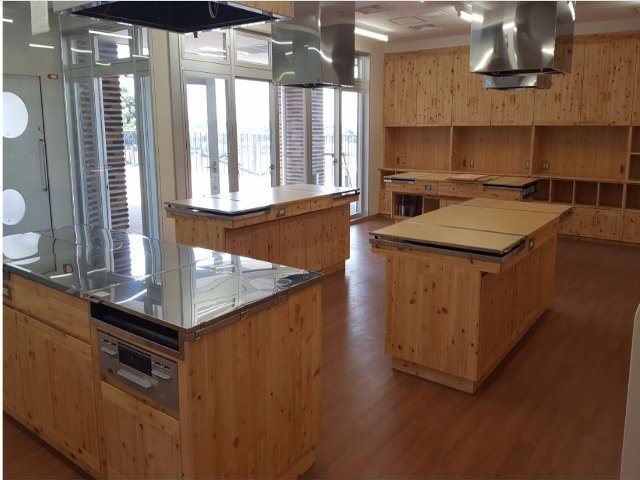 調理実習室左に窓ガラスと出入口があり、アルミ製の換気口と調理台以外が木材で施された調理実習室の写真