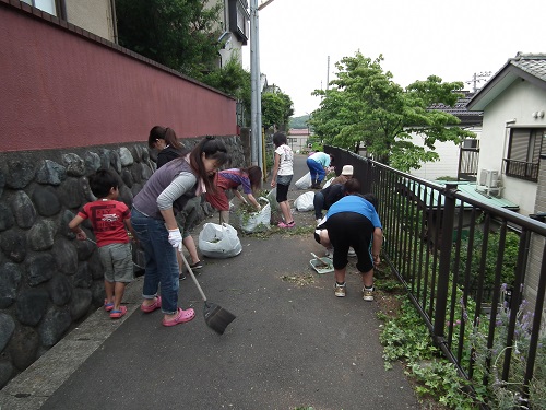 道路の雑草や落ち葉を集めてごみ袋に回収している清掃参加者の写真