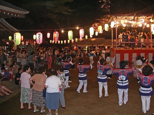 提灯の明かりに照らされて櫓の周りに集まって踊っている祭りの参加者の写真