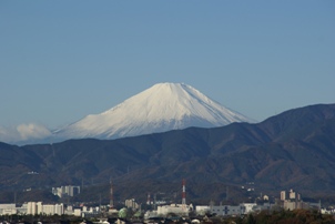 街並みと山脈の奥に、雪化粧姿の富士山が見えている写真