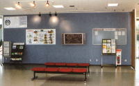 奥の壁に掲示板、左右にパンフレットスタンドが設置され、手前に4人掛けのベンチが設置されている情報コーナーの写真