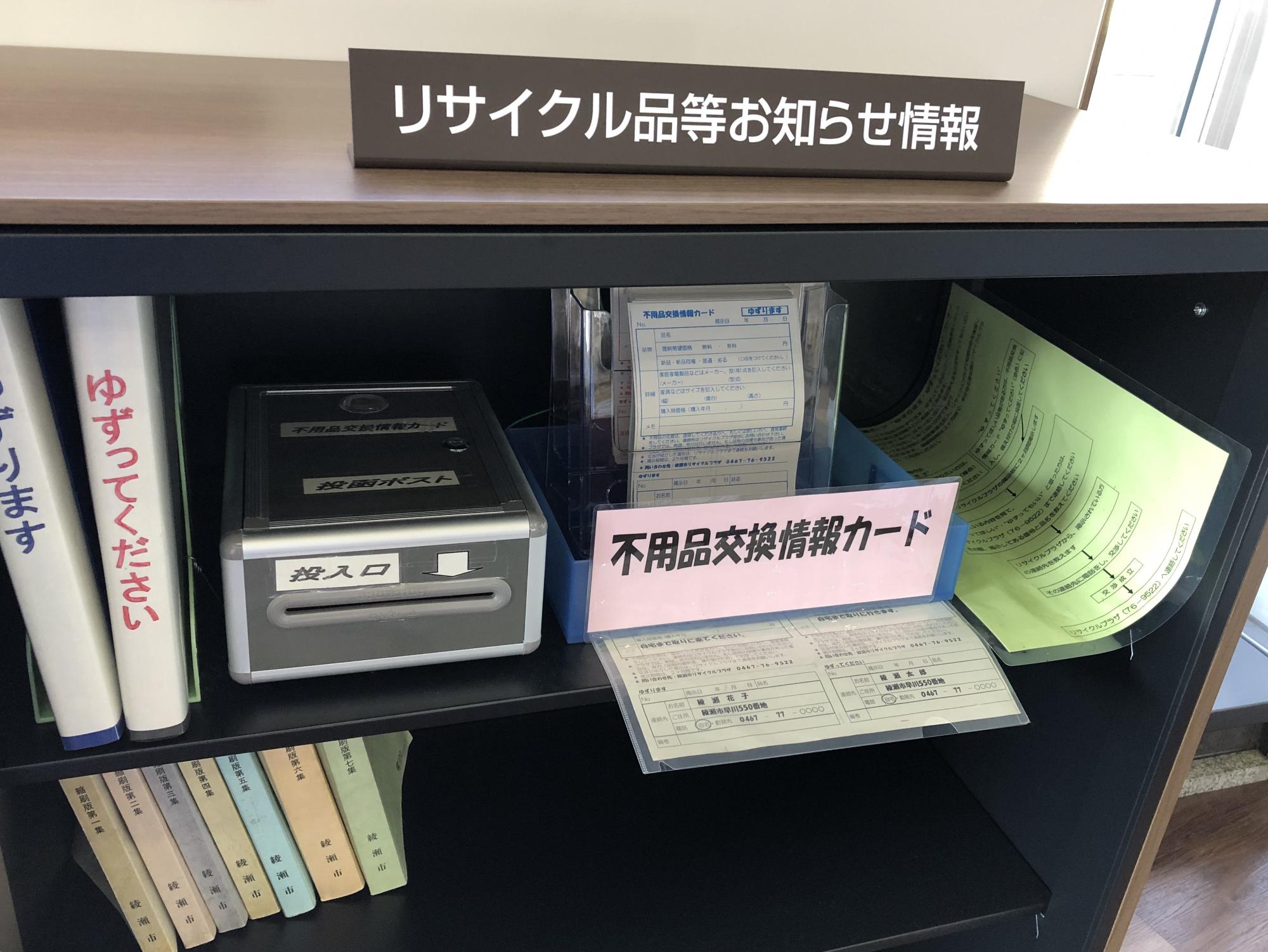 リサイクル品等お知らせ情報と書かれた机上札が置かれ、机の棚に不用品交換情報カードや投函ポストが置いてある写真