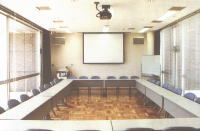 奥の壁際にスクリーン、部屋いっぱいに長机がロの字の形に設置された研修室の写真