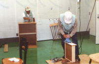 左奥の男性が棚を、右手前の男性が引き出しを修理している修理再生工房の写真