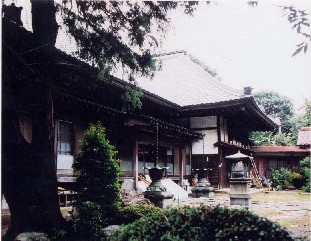 庭に石灯篭があり、大きな樹木の奥に瓦屋根で木造の済運寺が見える済運寺（さいうんじ）外観の写真