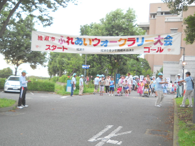 綾瀬市ふれあいウォークラリー大会 スタート ゴールと書かれた横断幕が掲げられ、多くの参加者で賑わっている様子の写真