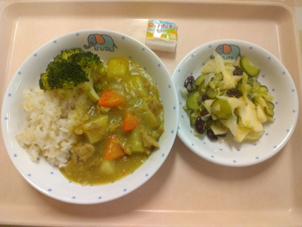 左に市内産ブロッコリーをトッピングしたカレーライス、右にりんごのコールスローサラダ、中央奥にチーズがトレーにのっている写真