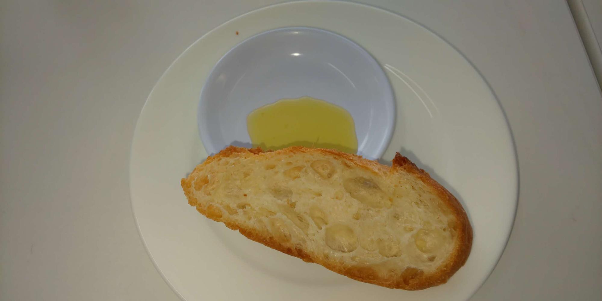 小皿に入ったオリーブオイルが白い皿にスライスされたフランスパンに添えてある写真