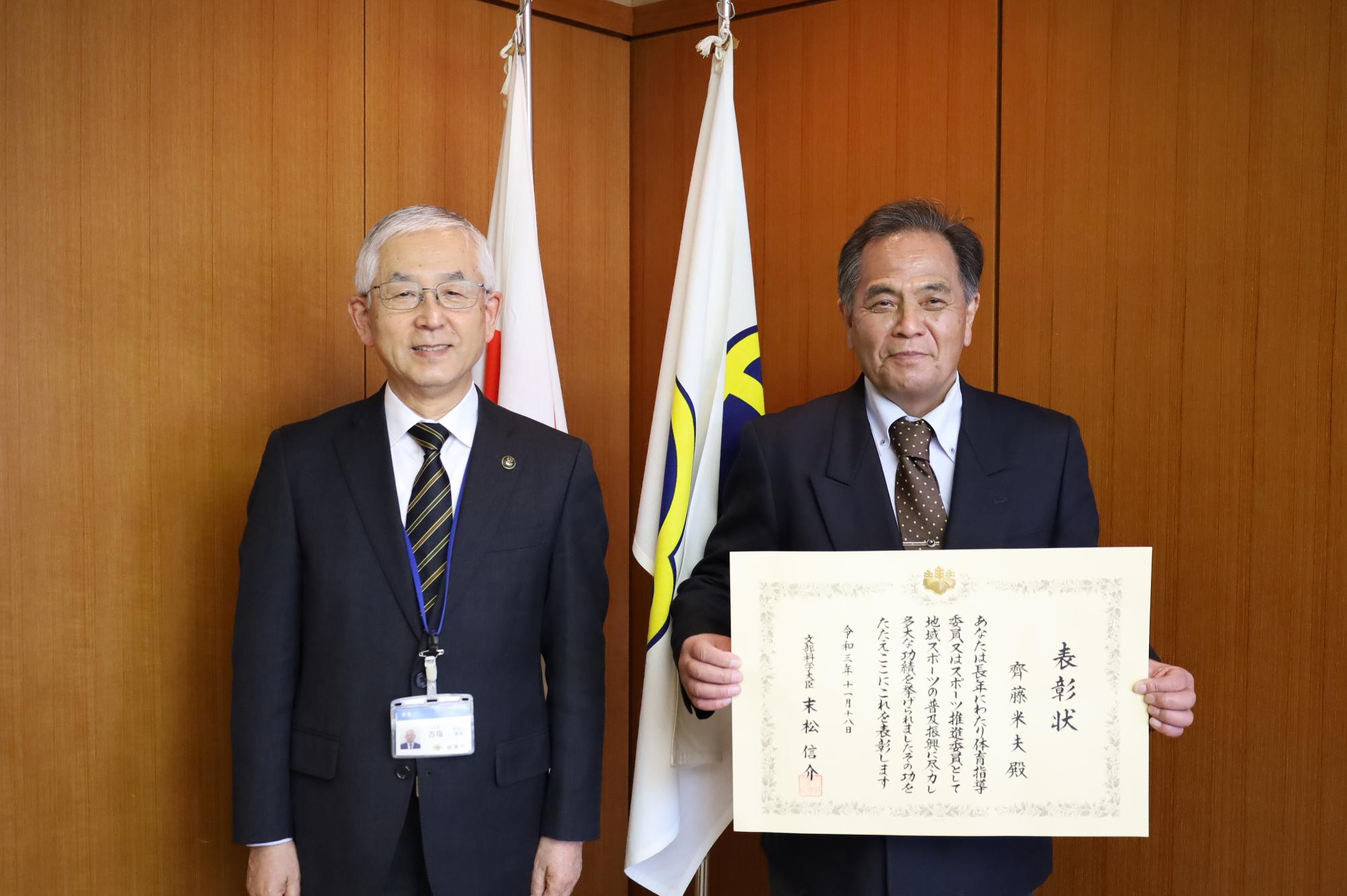 綾瀬市市長(左)と表彰状を両手で胸の位置で持っている齊藤米夫さん(右)の写真