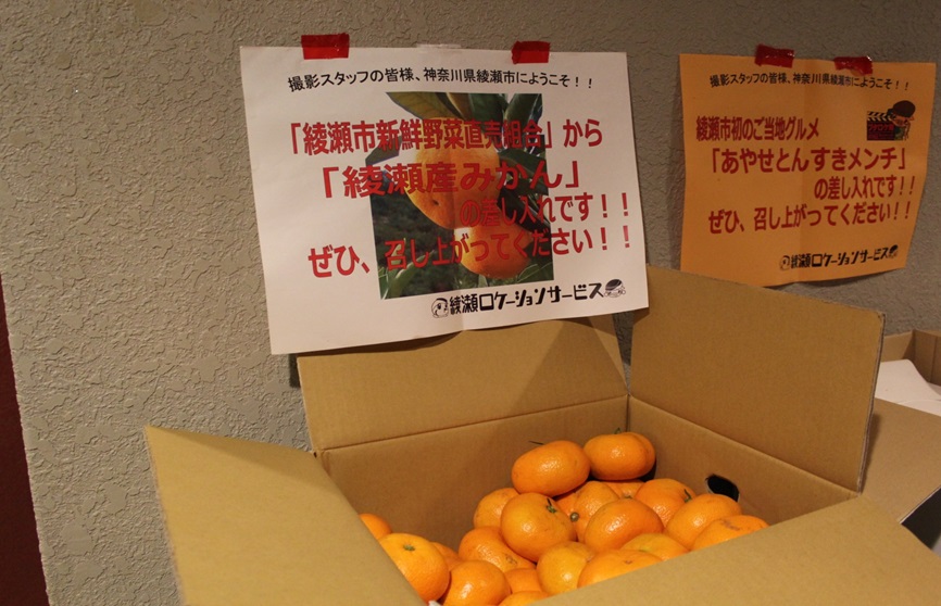 「綾瀬市新鮮野菜直売組合」から「綾瀬産みかん」の差し入れです。ぜひ、召し上がってください。と書かれた紙と段ボール箱いっぱいに入った、みかんの写真