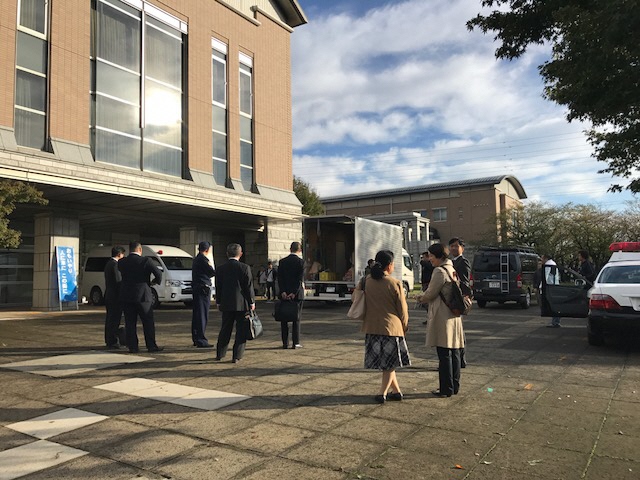 大きな建物の前の広場でスーツを着た男性や、女性の方が立っている写真