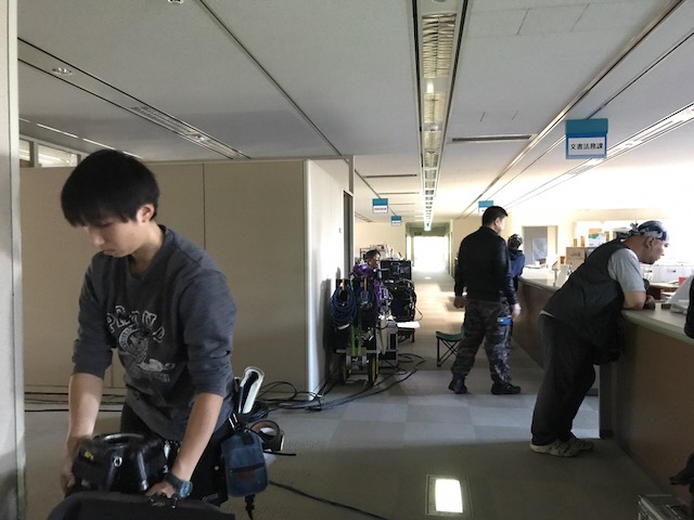 文書法務課の前に置かれた撮影機材や、周りで作業を行っている人々の写真