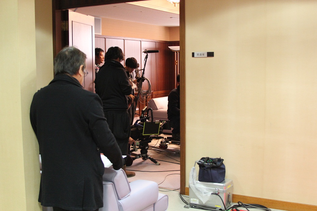 社長室のセット内にスタッフが機材や革張りのソファを運んでいる写真