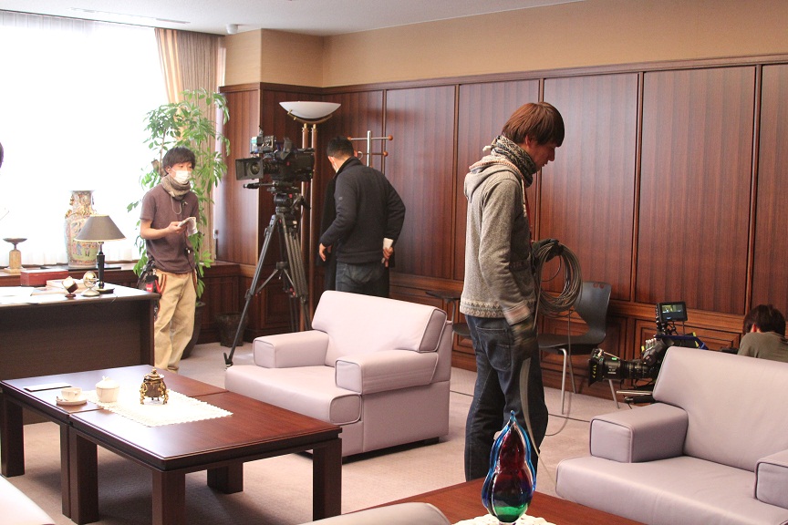 革張りのソファやテーブルなどが設置された社長室内で2台のカメラをセッティングしているスタッフの写真