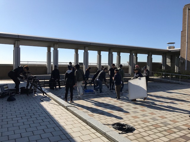 青空の下、屋外で、撮影機材が置かれ、スタッフの方々が作業をしている様子の写真