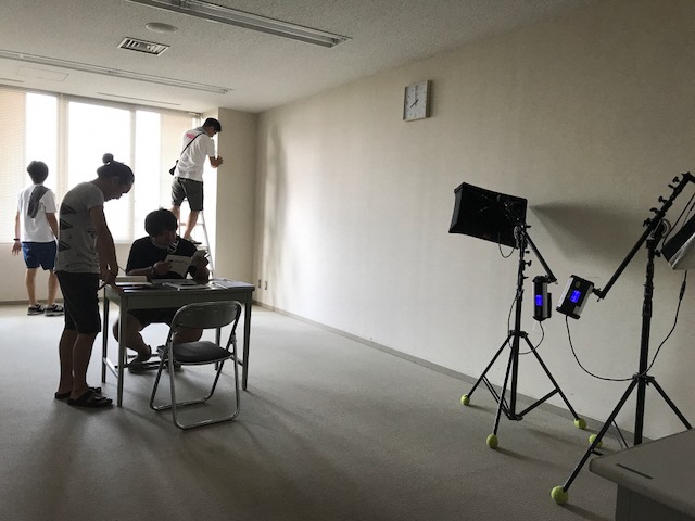 取調室のような部屋で4名のスタッフの方々が撮影の準備をしている写真