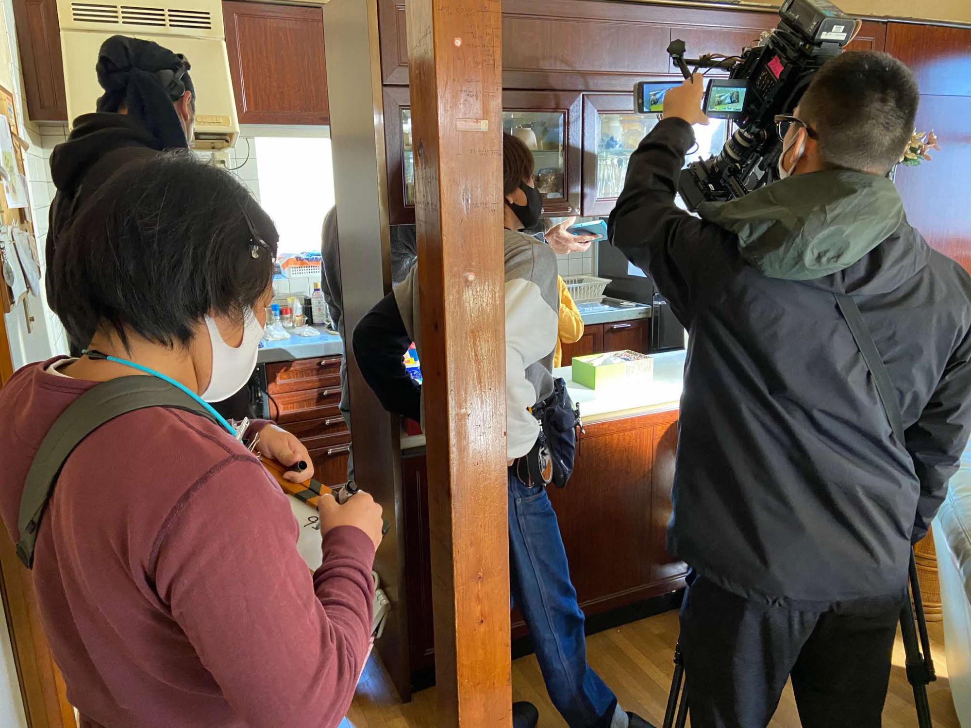 家の中のキッチンで、カメラを構えているスタッフ、ペンでカチンコに書き込みをしているスタッフの方などがいる撮影現場の写真