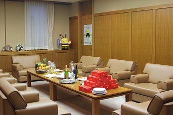 中央のテーブルに包装された品物や飲み物、食べ物がセットされ、周りにソファーが並べられた撮影時の市役所内の部屋の写真