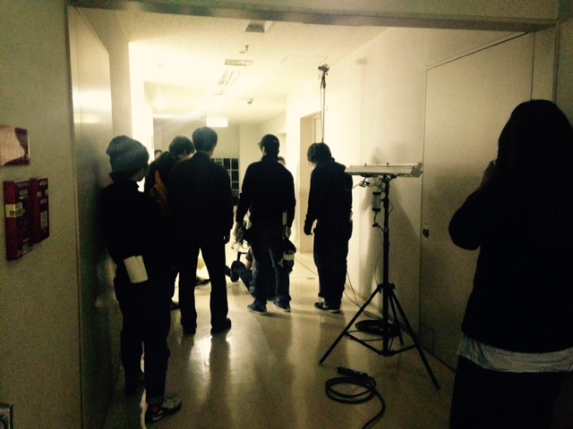数名の撮影スタッフが集まり廊下奥に照明を照らし撮影を行っている様子を後方から写した写真