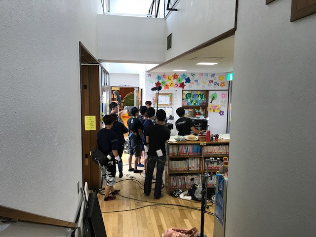児童館内の絵本が並んでいる棚の前に撮影機材が入り、スタッフの方々が撮影を行っている様子の写真
