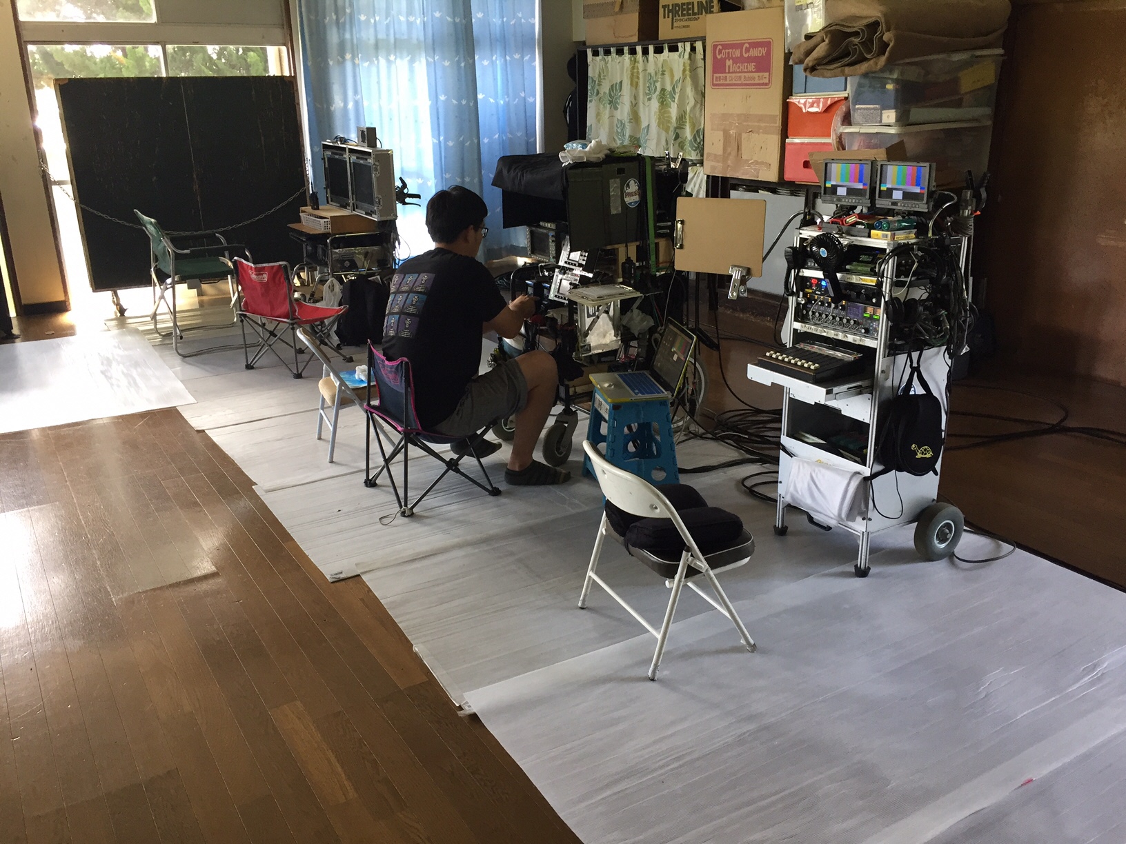 室内の一角に色々な撮影機材が置かれており、一人のスタッフの男性が椅子に座って、モニターを見ながら映像の確認をしている写真
