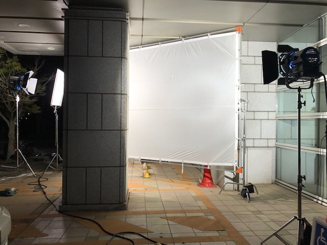 柱の奥に白い大きな布がかけられ、その布に照明をあてている撮影現場の写真