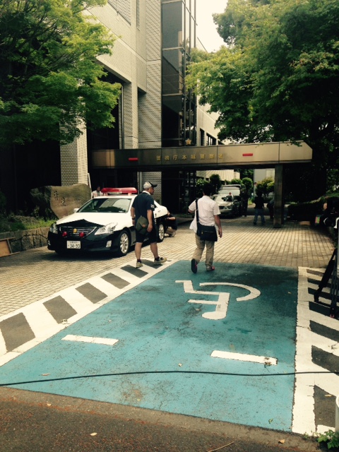 建物の手前に駐車しているパトカーの右側を2名のスタッフが歩いている写真