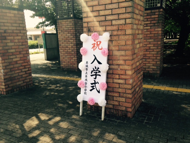 レンガ造りの柱に祝入学式と書かれ白とピンク色の花で飾られた看板が立て掛けられている写真