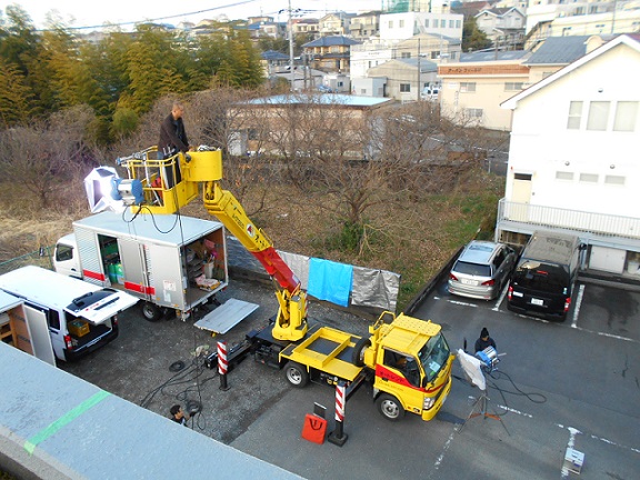ゴンドラに男性が乗っている撮影用のクレーン車を建物の屋上から撮影した写真