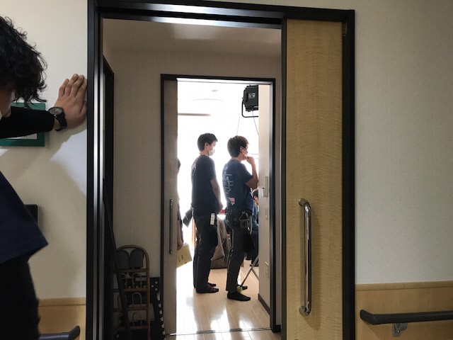室内で撮影が行われており、スタッフの方々が撮影している様子を廊下の入り口から写した写真