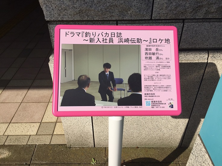 「釣りバカ日誌～新入社員浜崎伝助～」ロケ地の文字とスーツを着た俳優の濱田 岳さんが面接を受けているドラマの一場面を写したロケ地看板の写真