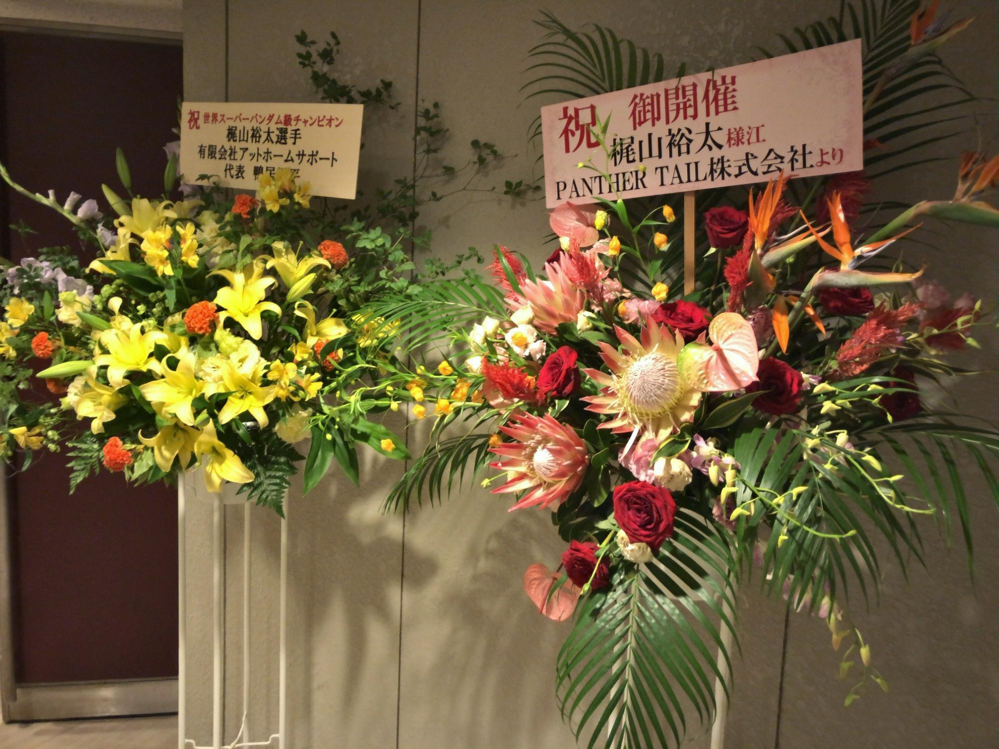 左に黄色とオレンジ色の花で生けられたスタンド花、右は赤色やピンク色の花でいけられたスタンド花をアップで撮影した写真