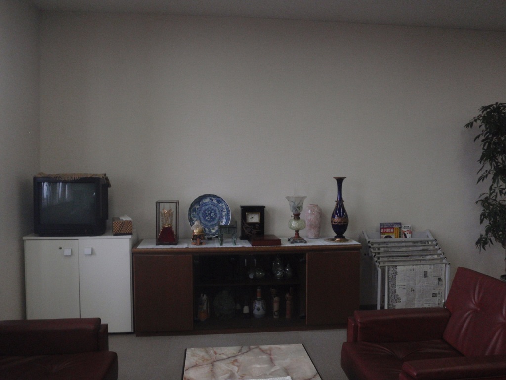 壁側に置かれた収納棚の上にテレビや壺、お皿などが置かれ、手前には応接セットのソフアと机が置かれている撮影現場の写真