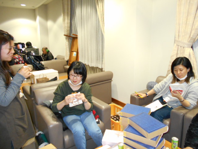 女性スタッフ3名がソファーに座り、あやせとんすきメンチを食べながらくつろいでいる様子の写真