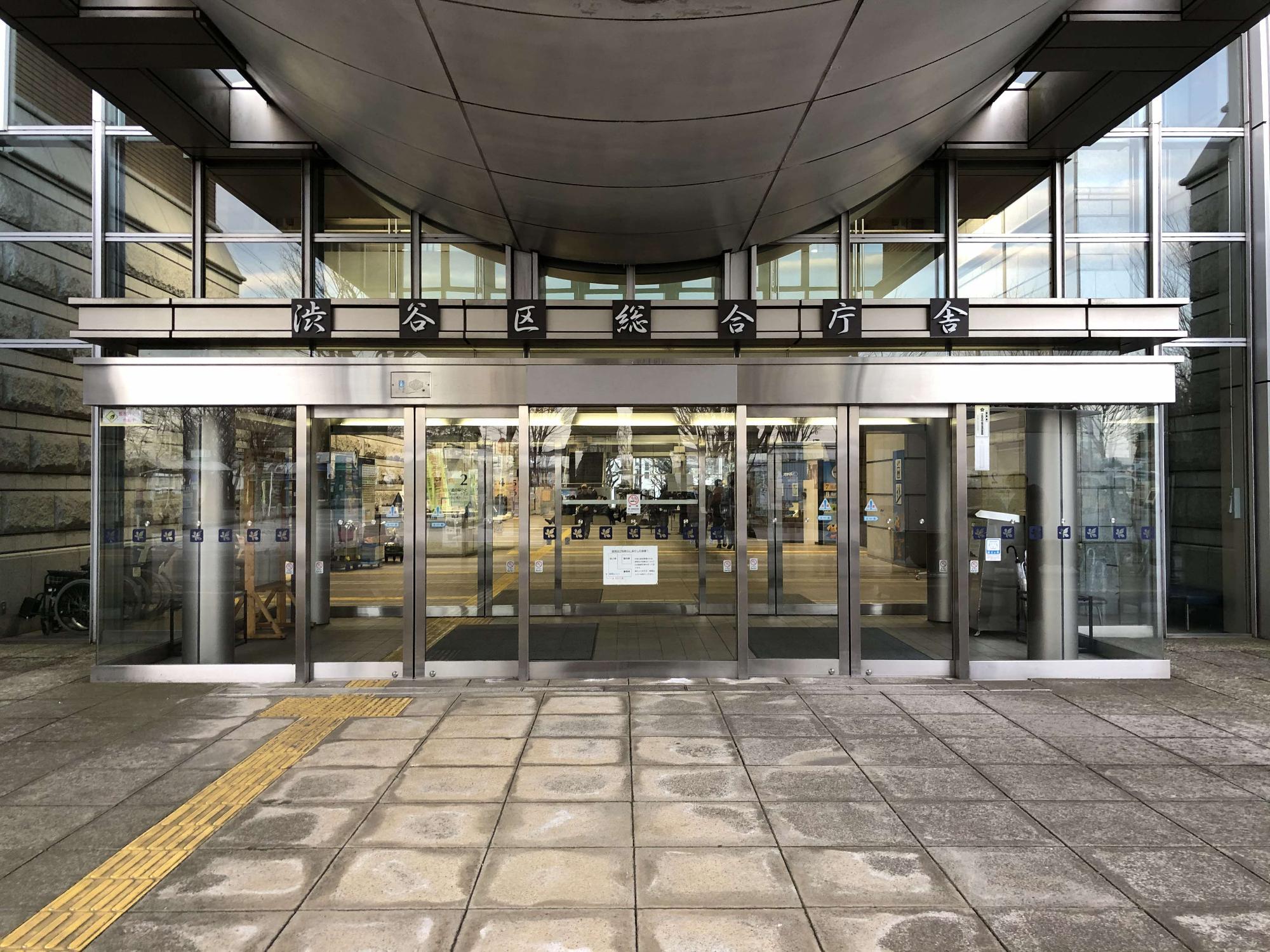 シルバーのフレームと全面ガラス張りで出来た入口上部に「渋谷区総合庁舎」と書かれた表示がある建物正面入口の写真