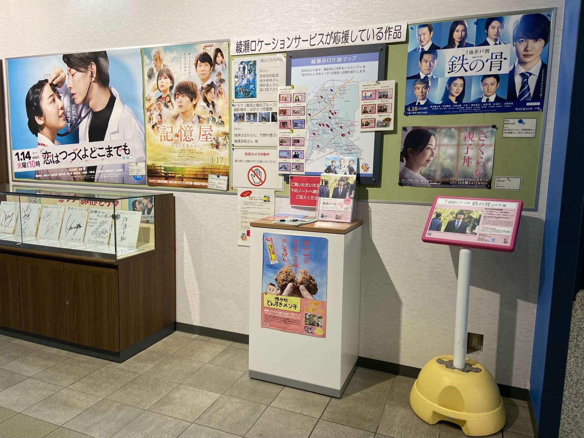 綾瀬ロケーションサービスが応援している作品のポスターが貼ってある掲示版前に置かれているロケ地看板が設置されている様子の写真