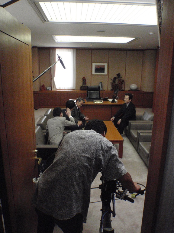 奥で演技をしている俳優さん達を入り口から撮影しているカメラマンさんの背中側から写した写真