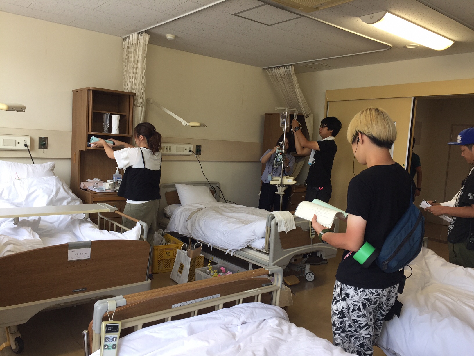 4台のベットがある病室で、スタッフの方が点滴の道具や棚にタオルを並べるなど撮影の準備をしている様子の写真