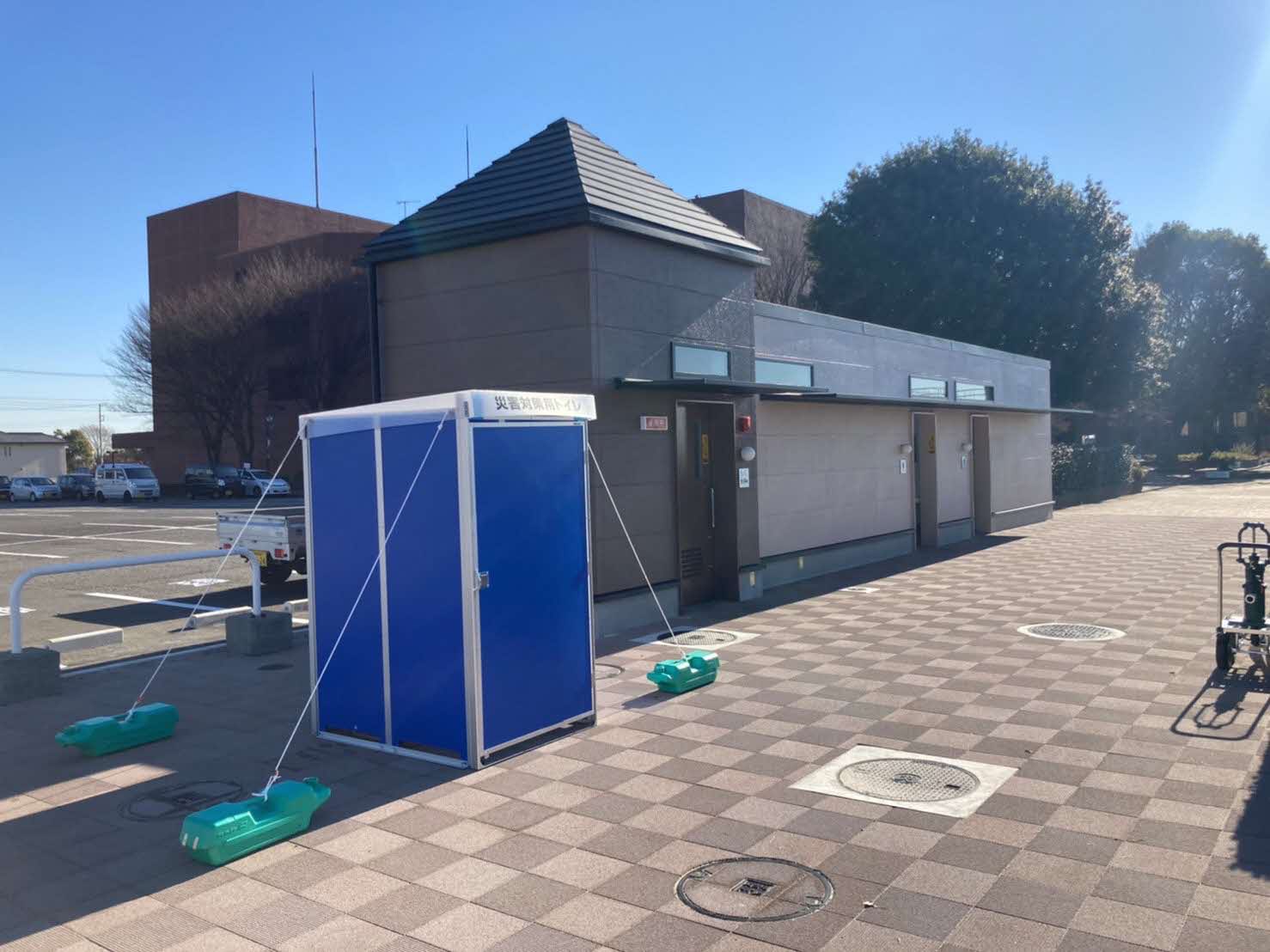 青色で箱型の建屋が設置され、四隅を重りで固定しているマンホールトイレの建屋の写真