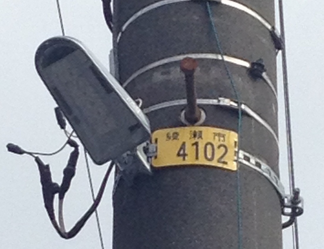 点灯していないLED防犯灯と「綾瀬市4102」と書かれた黄色いプレートをアップで撮影した写真