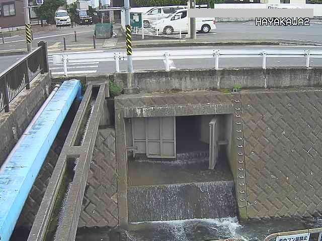 左側の橋と奥の道路の境目の川の壁に川に向かって流れてくる排水路がある場所に設置されたライブカメラ映像の写真