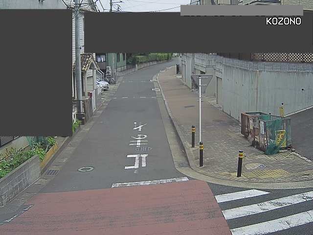 住宅地に挟まれた細い道路が手前に向かって傾斜になっている交差点がある場所に設置されたライブカメラ映像の写真