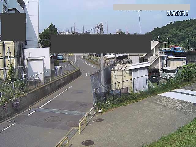 左側に工場の様な建物と右側にトラックが停まっている2階建ての事務所の敷地の間にくの字に折れた坂道があり、手前から右側にYの字に上がっていく傾斜の道ある場所に設置されたライブカメラ映像の写真